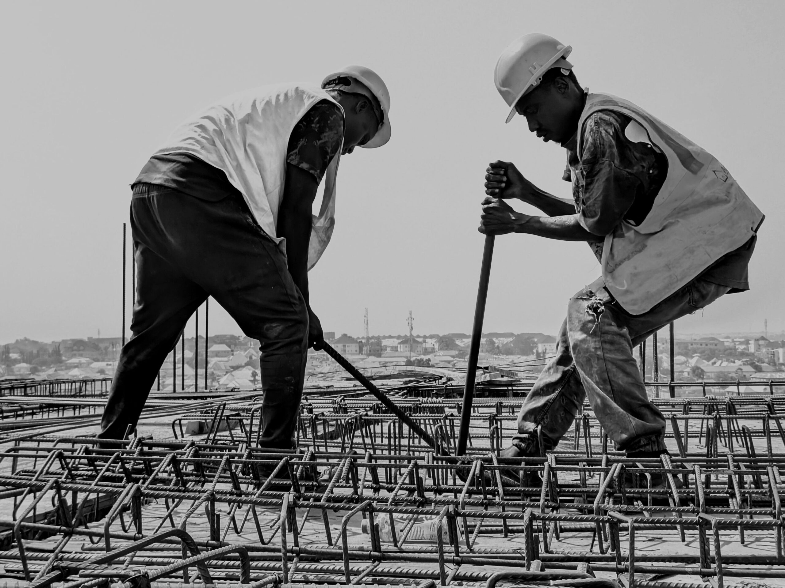 New info Black and white image of two construction workers reinforcing steel bars on a building site.