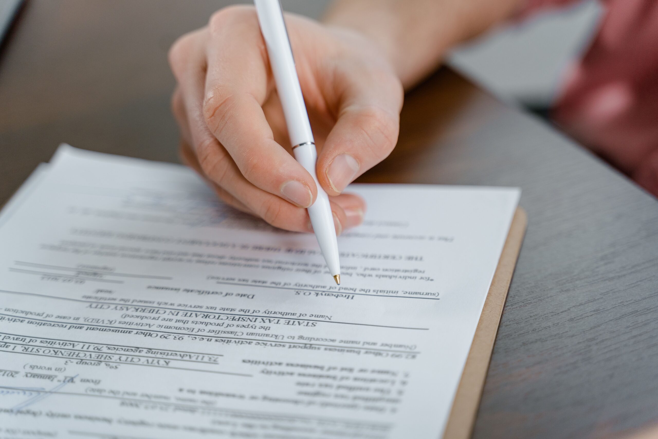 New info A hand holding a pen signing a document, close-up shot with focus on the paper.