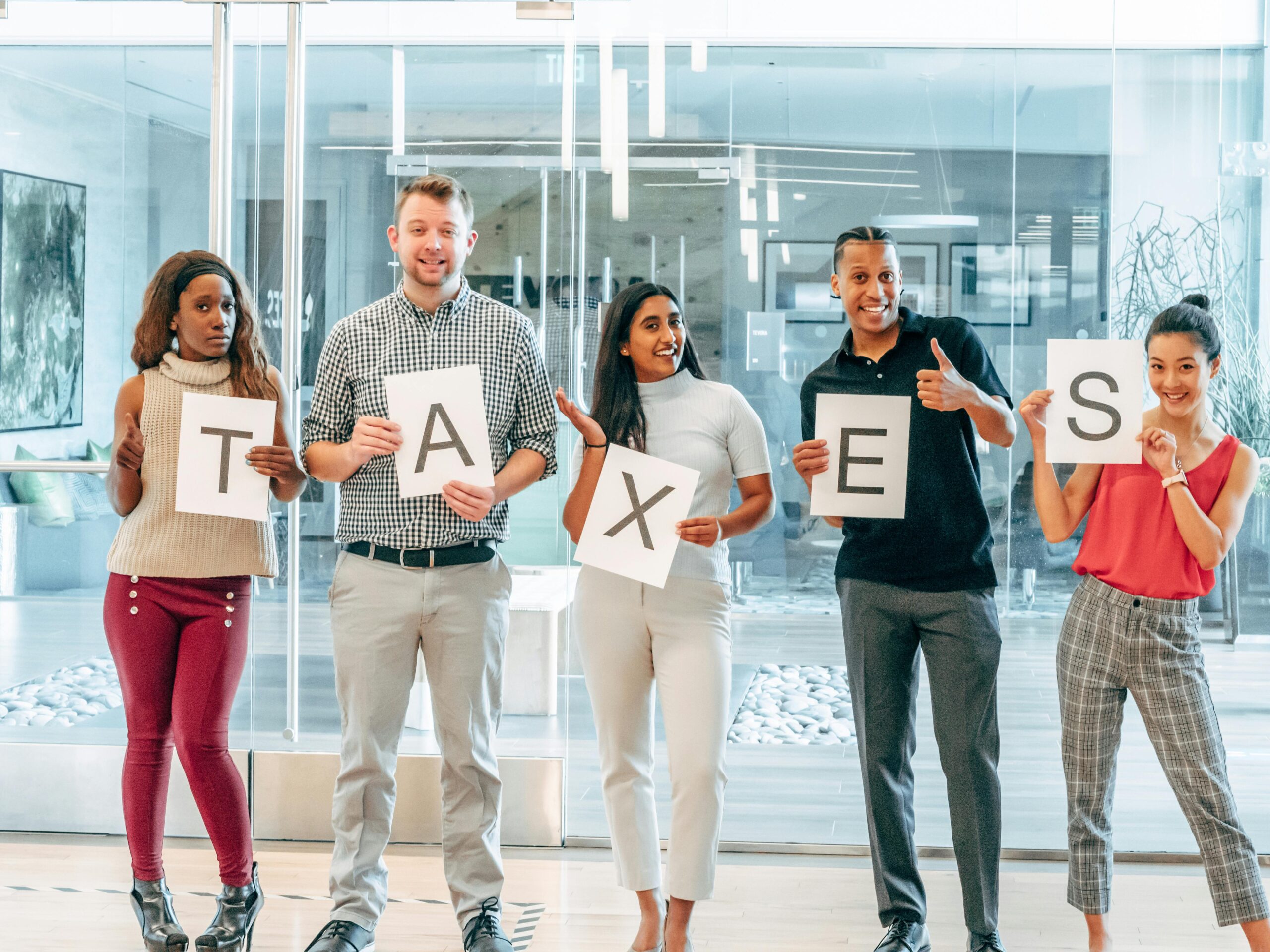 New info A diverse group of adults holding letters that spell 'taxes' inside an office setting.